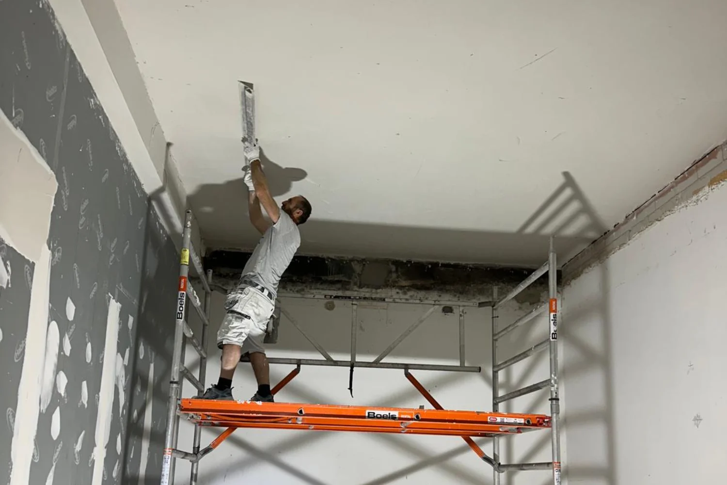 Man plasters ceiling on scaffolding indoors